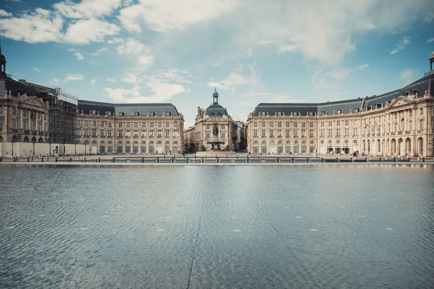 Place de la Bourse et miroir d'eau à Bordeaux sous un ciel bleu, sans passants.