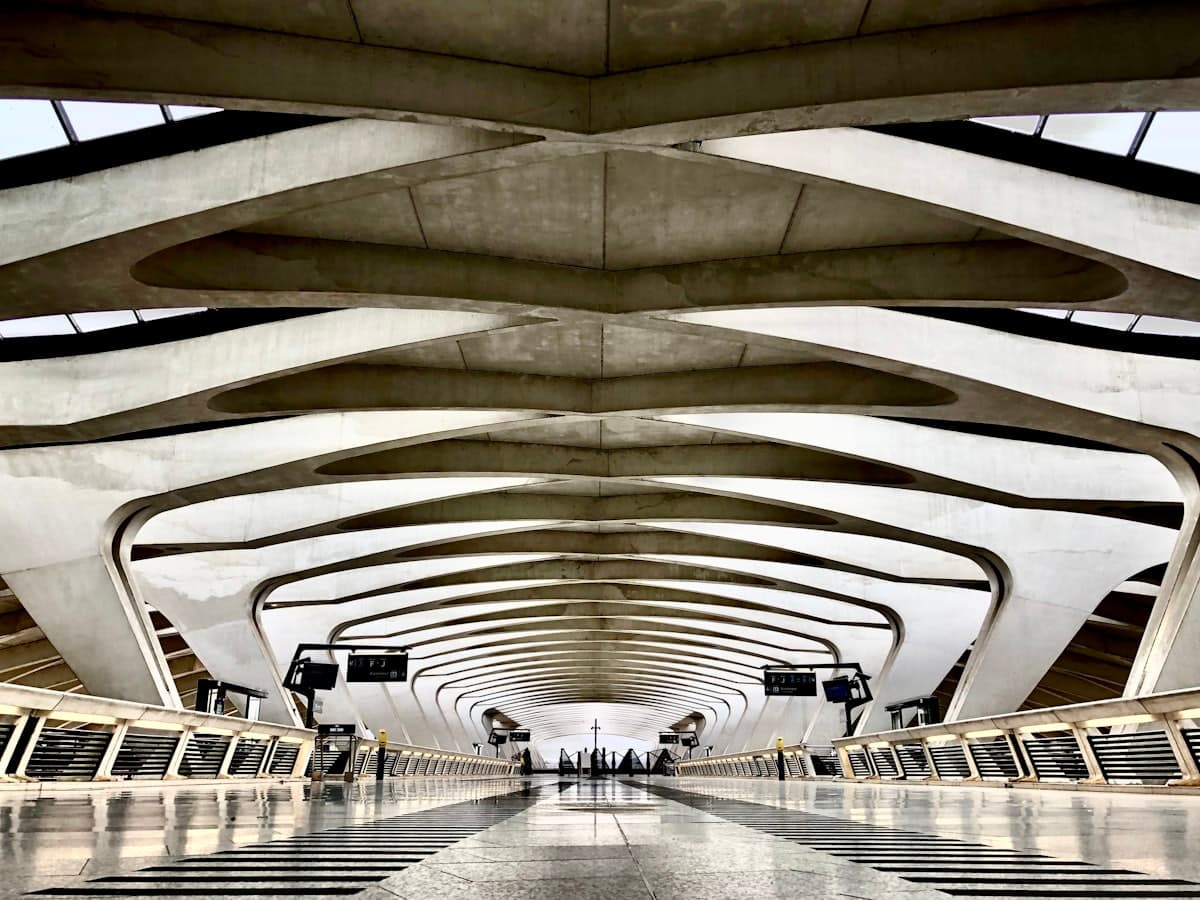 Hall voûté d'une gare ferroviaire contemporaine, quais déserts sous une verrière lumineuse.