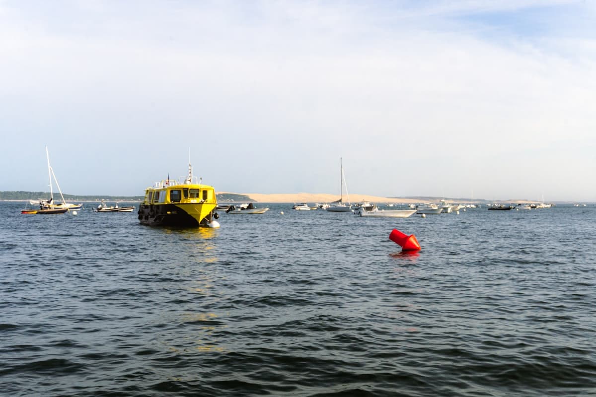 Bassin d'Arcachon avec la dune du Pilat à l'horizon et des bateaux ostréicoles amarrés.